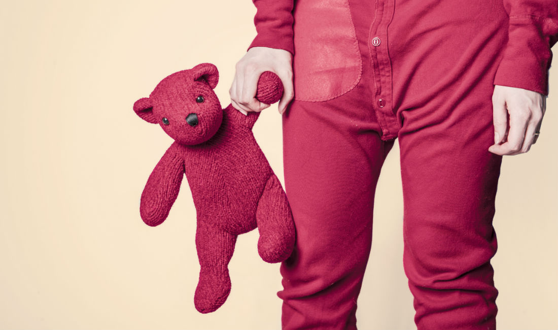 Ragazza con pigiama intero rosa e orsacchiotto in mano