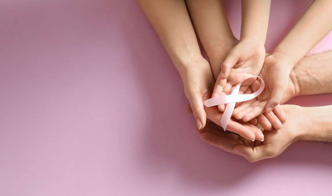 Mani femminili una sull'altra reggono un fiocco rosa simbolo di prevenzione per la salute della donna