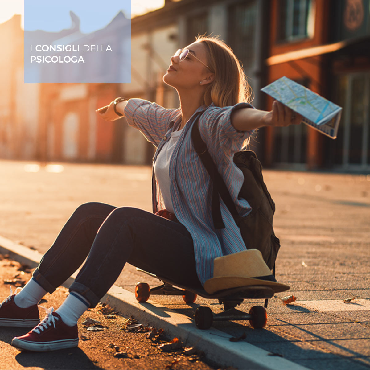 Una ragazza allarga le braccia al sole seduta su uno skateboard