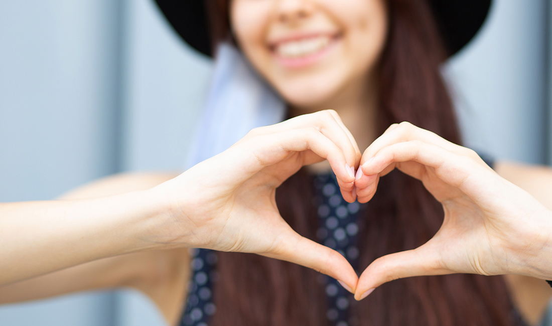 ragazza sorridente con mascherina sull'orecchio fa un cuore con le dita