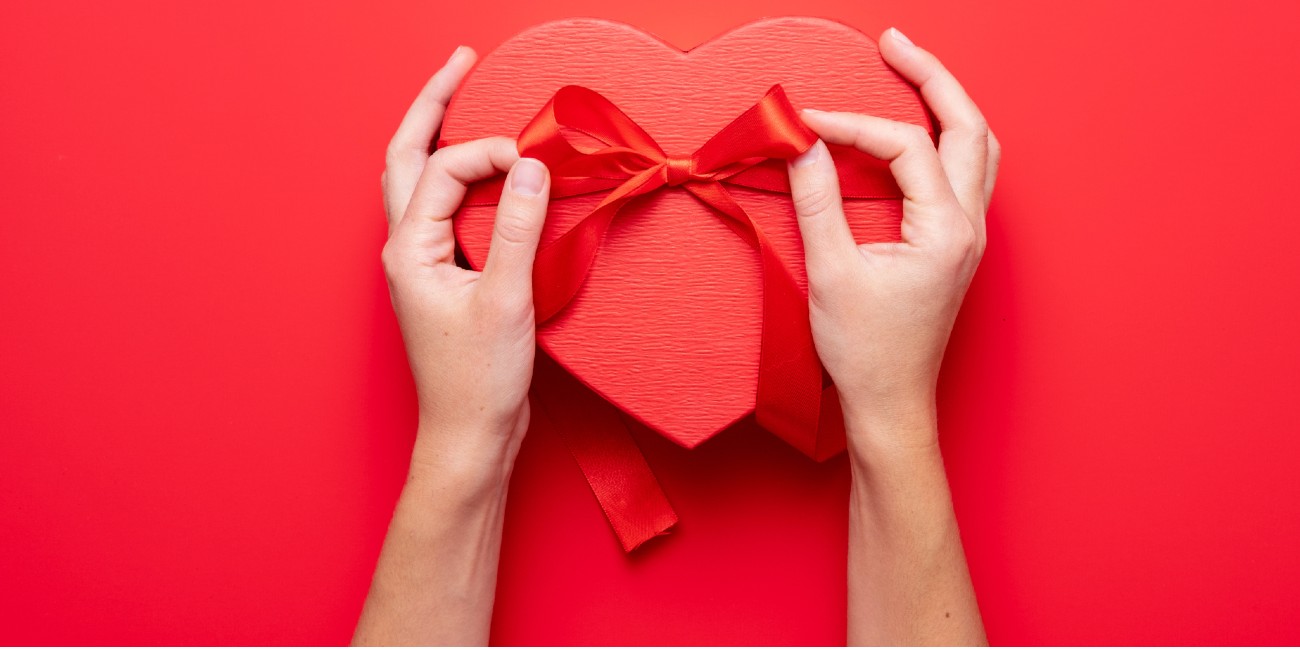 Regali di coppia per San Valentino: mani femminili confezionano un pacchetto a forma di cuore