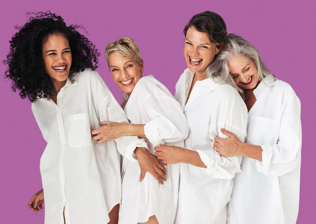 Concept per salute delle donne: quattro donne di età differenti, sorridenti, con camicia bianca - Magazine Femminile