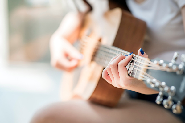 Concept per attività da fare nel tempo libero: close up su mani di donna che suonano la chitarra