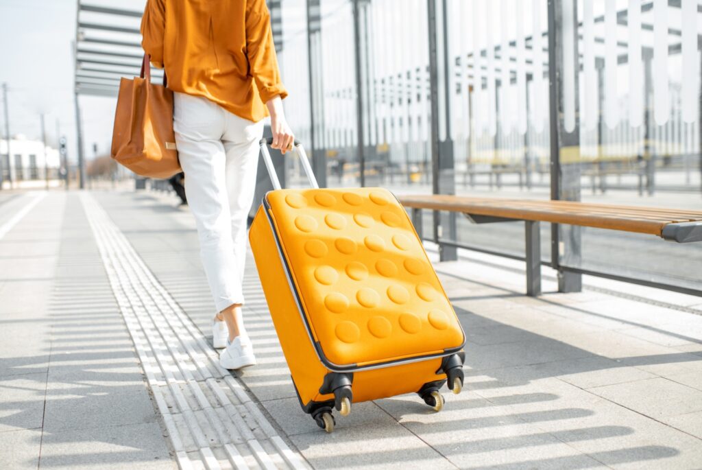 Concept per consigli per viaggiare da sola: close up su donna che tira una valigia gialla in una stazione