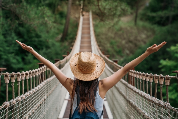 Concept per consigli per viaggiare da sola: giovane donna fotografata di schiena e in procinto di attraversare un ponte di corda